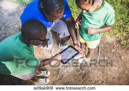 Stock Photo - Father with daughter and son navigating with digital tablet at eco camp. Fotosearch