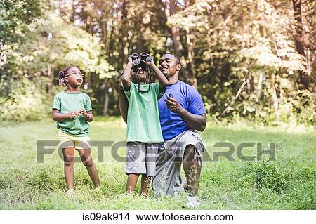 Picture - Father with son and daughter bird watching in eco forest camp. Fotosearch