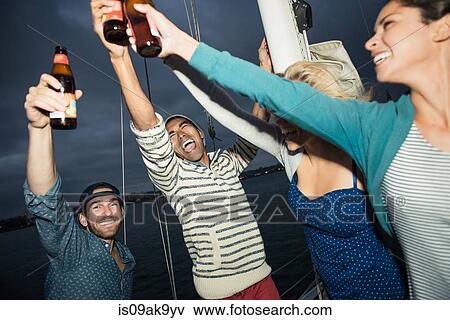 Stock Photo - Friends toasting with beer bottles on sailing boat. Fotosearch