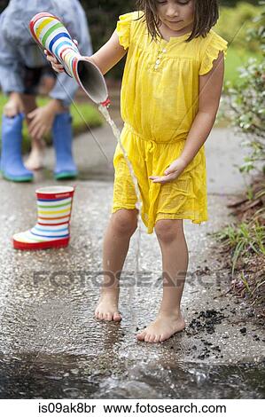 Stock Photography - Girl pouring water from rubber boots into rain puddle. Fotosearch