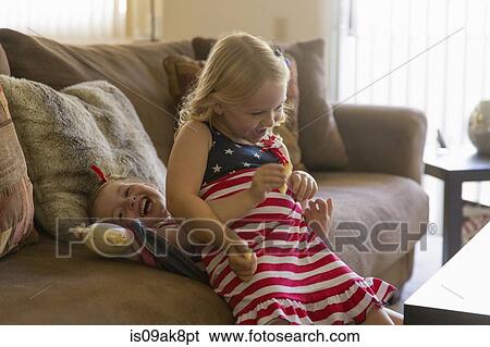 Stock Photograph - Girl sitting on top of older sister on sofa. Fotosearch