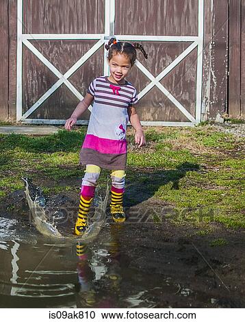 Stock Image - Girl stamping and splashing in garden puddle. Fotosearch