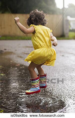 Stock Photograph - Girl wearing rubber boots jumping in rain puddle. Fotosearch
