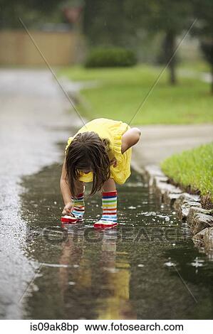 Girl wearing rubber boots picking leaf from rain puddle View Large Photo Image Stock Photography - Girl wearing rubber boots picking leaf from rain puddle. Fotosearch