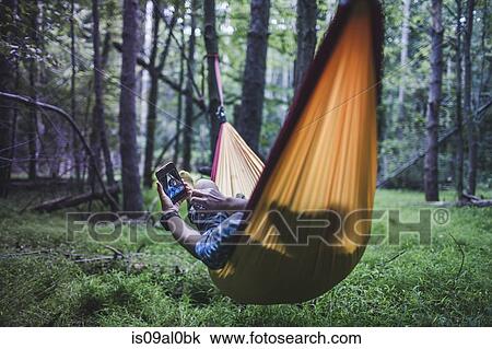 Hiker lying in hammock in forest using digital device View Large Photo Image Stock Image - Hiker lying in hammock in forest using digital device. Fotosearch
