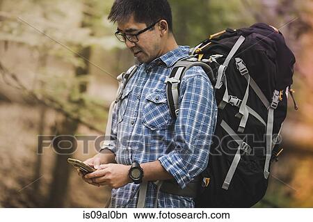 Hiker with backpack, looking at smartphone View Large Photo Image Picture - Hiker with backpack, looking at smartphone. Fotosearch