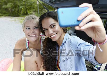 Stock Photograph - Hikers sitting at rear of car taking selfie. Fotosearch