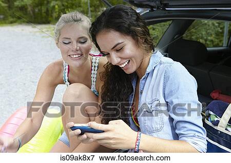 Stock Photo - Hikers sitting at rear of car using smartphone. Fotosearch