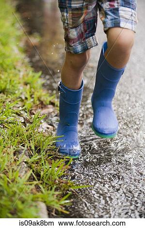 Picture - Legs of boy running wearing rubber boots. Fotosearch