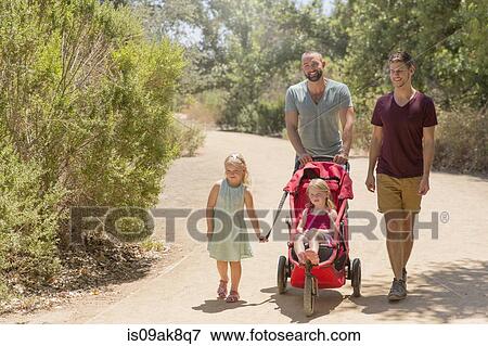 Stock Photo - Male couple strolling with two daughters in park. Fotosearch