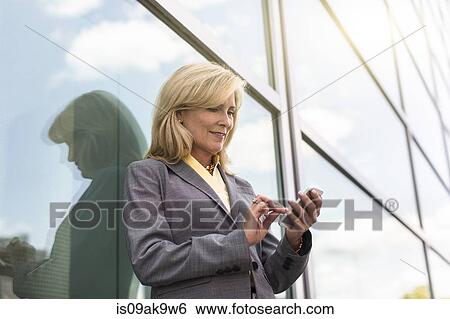 Mature businesswoman outside building using smartphone View Large Photo Image Stock Photograph - Mature businesswoman outside building using smartphone. Fotosearch