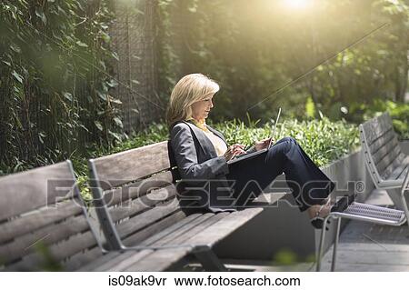 Stock Photography - Mature businesswoman sitting on bench using laptop. Fotosearch