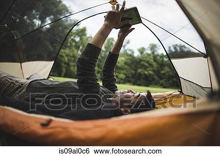 Stock Photograph - Mature man lying in tent using digital tablet. Fotosearch