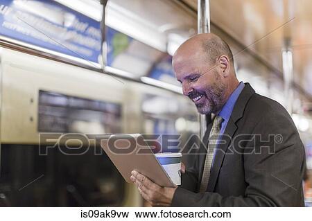 Stock Photo - Mature man on subway train holding digital tablet. Fotosearch