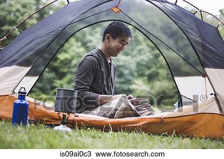 Stock Image - Mature man sitting in tent using digital tablet. Fotosearch