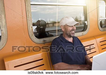 Stock Image - Mature man using laptop on passenger ferry. Fotosearch
