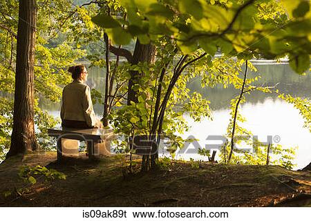 Stock Photograph - Mature woman sitting on lakeside seat in forest, Brattleboro, Vermont, USA. Fotosearch