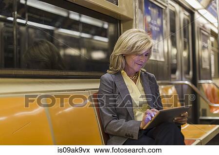 Mature woman sitting on subway train using digital tablet View Large Photo Image Stock Photo - Mature woman sitting on subway train using digital tablet. Fotosearch