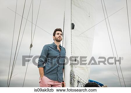 Stock Image - Mid adult man on sailing boat. Fotosearch