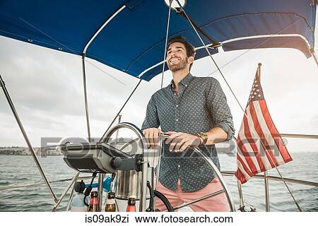 Stock Image - Mid adult man steering sailing boat. Fotosearch