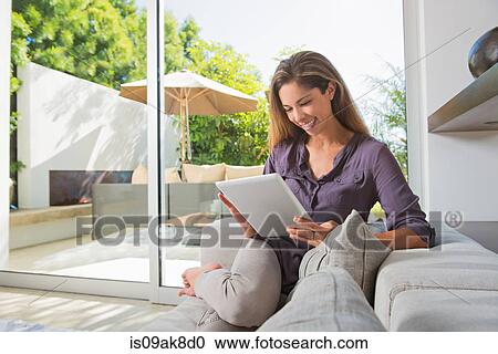 Mid adult woman using touchscreen on digital tablet on sitting room sofa View Large Photo Image Stock Image - Mid adult woman using touchscreen on digital tablet on sitting room sofa. Fotosearch