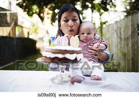 Mother holding baby son, blowing out candles on cake View Large Photo Image Stock Image - Mother holding baby son, blowing out candles on cake. Fotosearch