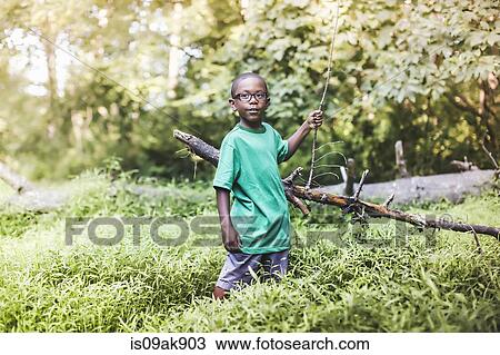 Stock Image - Portrait of boy touching fallen tree in forest eco camp. Fotosearch