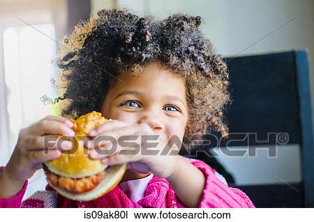 Portrait of cute girl eating hamburger in kitchen View Large Photo Image Stock Image - Portrait of cute girl eating hamburger in kitchen. Fotosearch