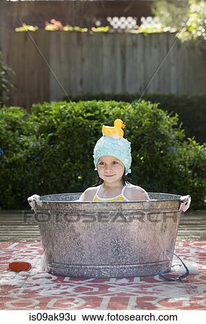 Stock Photograph - Portrait of girl in bubble bath in garden with rubber duck on head. Fotosearch
