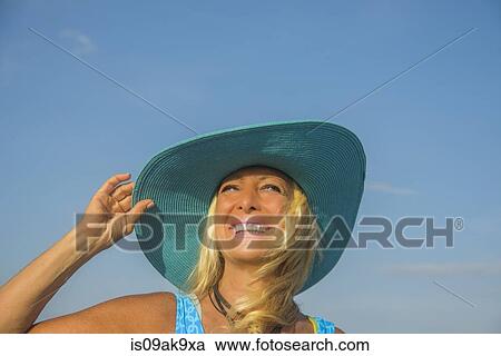 Stock Image - Portrait of smiling mature woman holding onto sunhat. Fotosearch