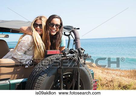Picture - Portrait of two young women leaning out of jeep at coast, Malibu, California, USA. Fotosearch