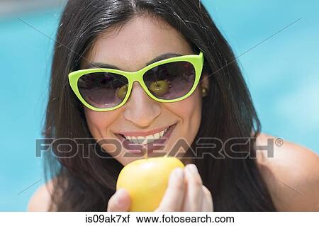 Stock Image - Portrait of young woman by pool holding up apple. Fotosearch