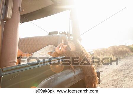 Stock Image - Portrait of young woman reclining in back seat of jeep at coast, Malibu, California, USA. Fotosearch