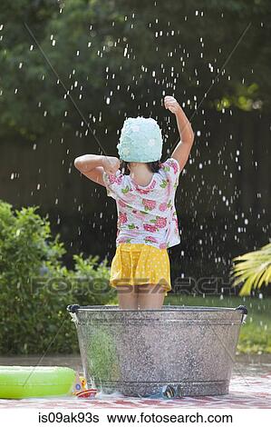 Stock Photograph - Rear view of girl standing in bubble bath in garden splashing soap bubbles. Fotosearch