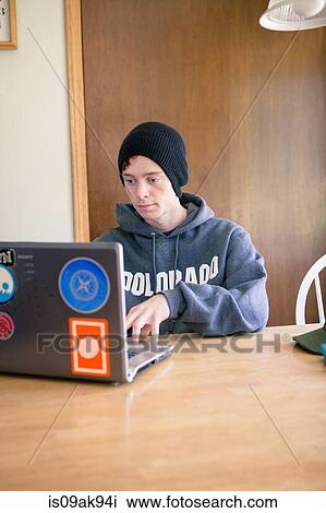 Teenage boy sitting at dining room table using laptop View Large Photo Image Stock Image - Teenage boy sitting at dining room table using laptop. Fotosearch