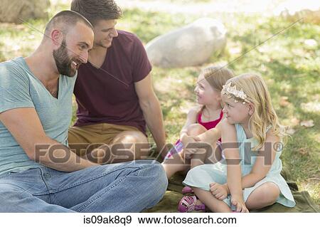 Stock Photo - Two sisters and fathers sitting chatting in park. Fotosearch