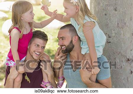 Stock Image - Two sisters sitting on fathers shoulders in park. Fotosearch