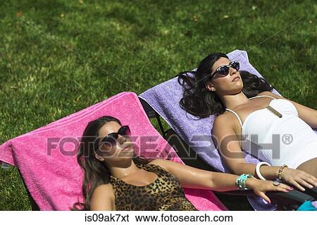 Two sisters sunbathing on loungers in garden View Large Photo Image Stock Photograph - Two sisters sunbathing on loungers in garden. Fotosearch