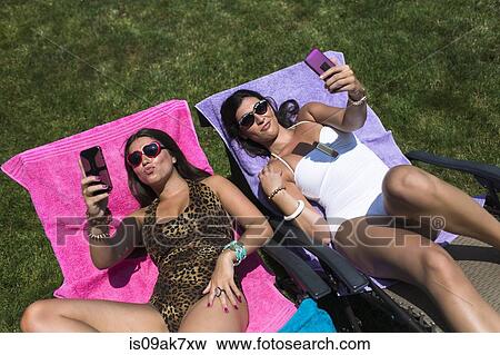 Two sisters taking selfies whilst sunbathing on loungers in garden View Large Photo Image Stock Photo - Two sisters taking selfies whilst sunbathing on loungers in garden. Fotosearch