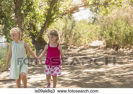 Two young sisters strolling and holding hands on riverbank View Large Photo Image Stock Image - Two young sisters strolling and holding hands on riverbank. Fotosearch