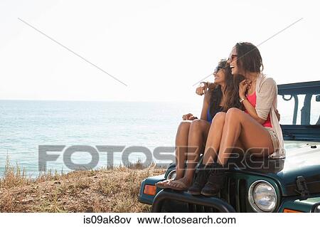 Two young women sitting on hood of jeep at coast, Malibu, California, USA View Large Photo Image Stock Photo - Two young women sitting on hood of jeep at coast, Malibu, California, USA. Fotosearch