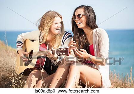 Stock Image - Two young women with acoustic guitar at coast, Malibu, California, USA. Fotosearch