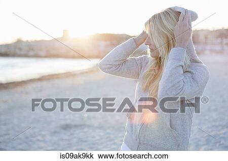Woman putting hood over head on the beach View Large Photo Image Stock Image - Woman putting hood over head on the beach. Fotosearch