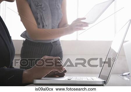 Woman using laptop, woman in background holding digital tablet View Large Photo Image Stock Photo - Woman using laptop, woman in background holding digital tablet. Fotosearch