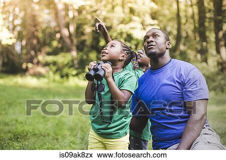 Stock Photo - Young father with son and daughter bird watching in eco forest camp. Fotosearch