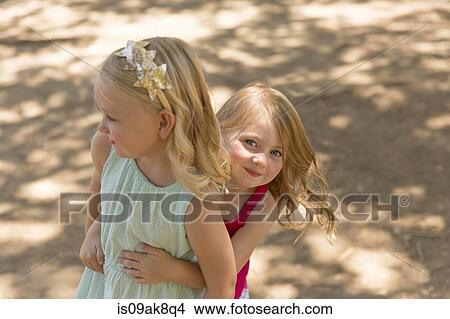 Picture - Young girl hiding behind sister in park. Fotosearch