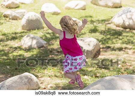 Stock Photo - Young girl jumping from boulders in park. Fotosearch