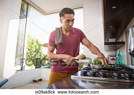 Stock Image - Young man cooking on hob in kitchen. Fotosearch