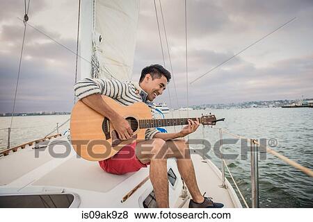 Stock Photo - Young man on sailing boat playing guitar. Fotosearch