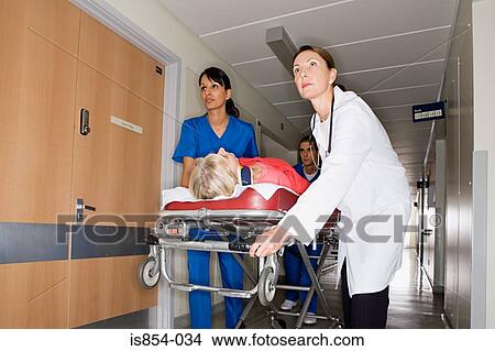 Picture - Doctors wheeling patient through corridor. Fotosearch
